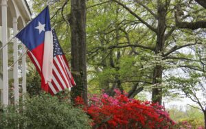 Historic house with Lone Star flag and US flag hanging from it with oak trees in the background. The house is in Tyler, one of the best day trips from dallas texas