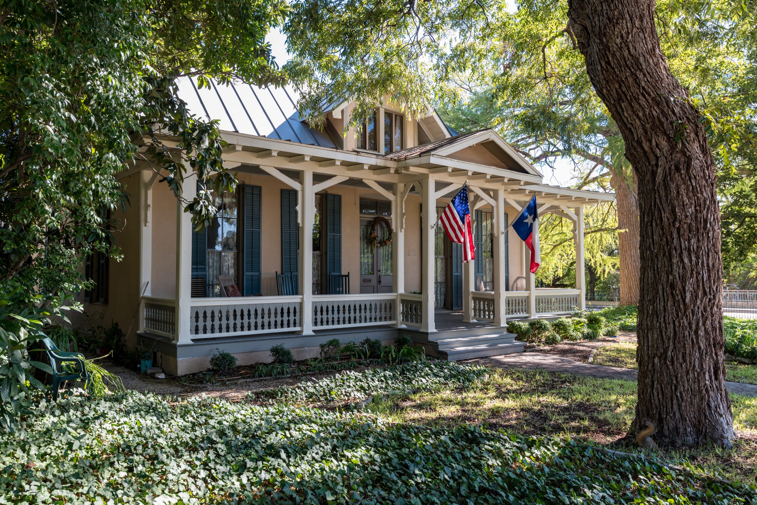 Texas house with a white front porch and black shutters shaded by a live oak tree in the King William Historic District San Antonio
