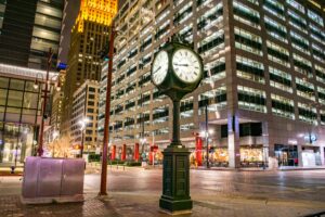 Downtown street in Houston TX at night with skyscrapers lining it and a clock in the foreground, dallas vs houston