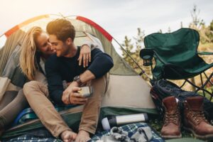 Young couple sititng inside a tent at a campsite, with a green camping chair next to them. There are plenty of fun places to camp near San Antonio Texas!